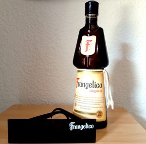 „Eine Flasche Frangelico Haselnusslikör auf einem Holztisch, davor liegt eine schwarze Balken-Sonnenbrille mit dem weißen Markenlogo.“